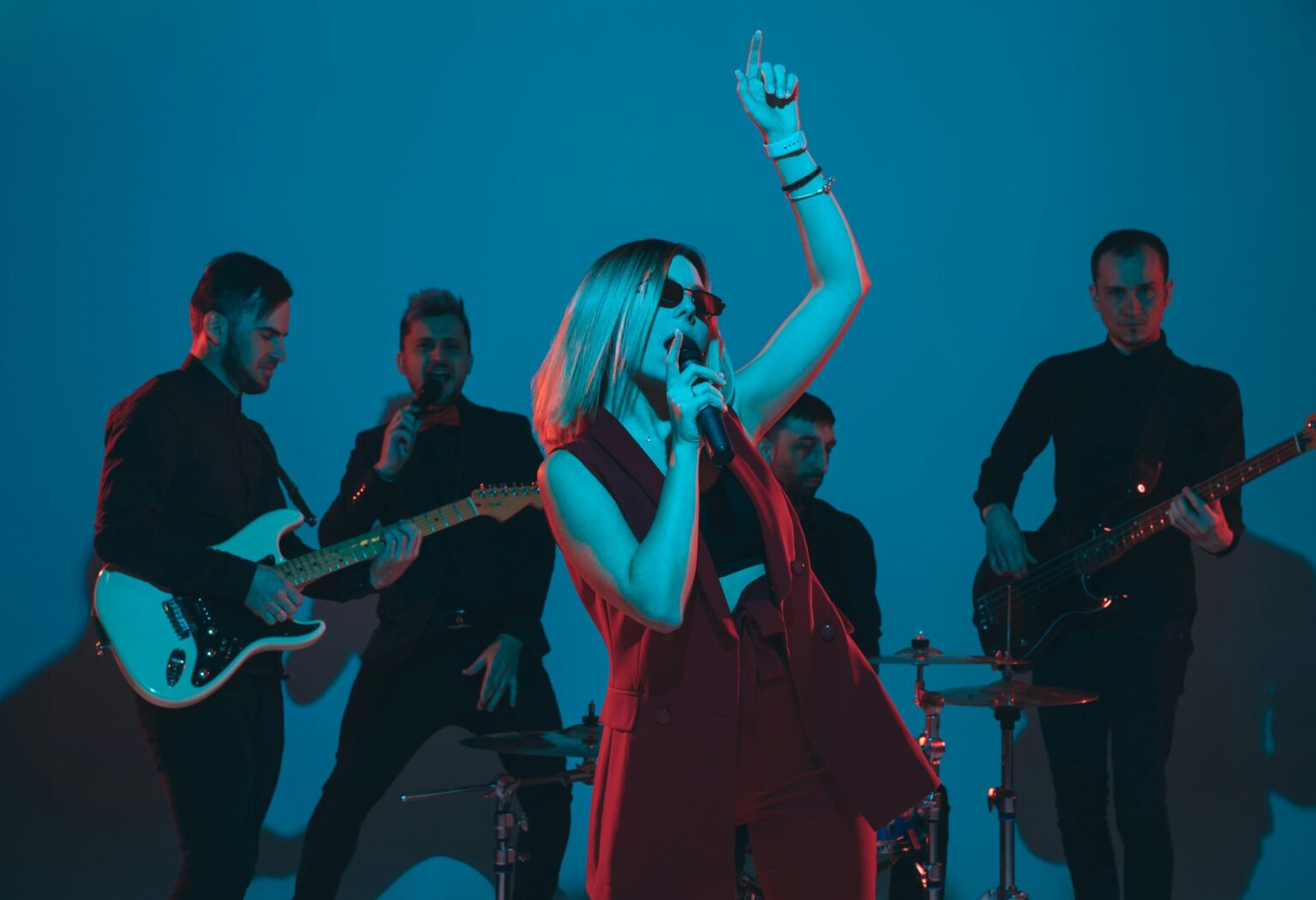 Young caucasian musicians, band performing in neon light on blue studio background, singer in front